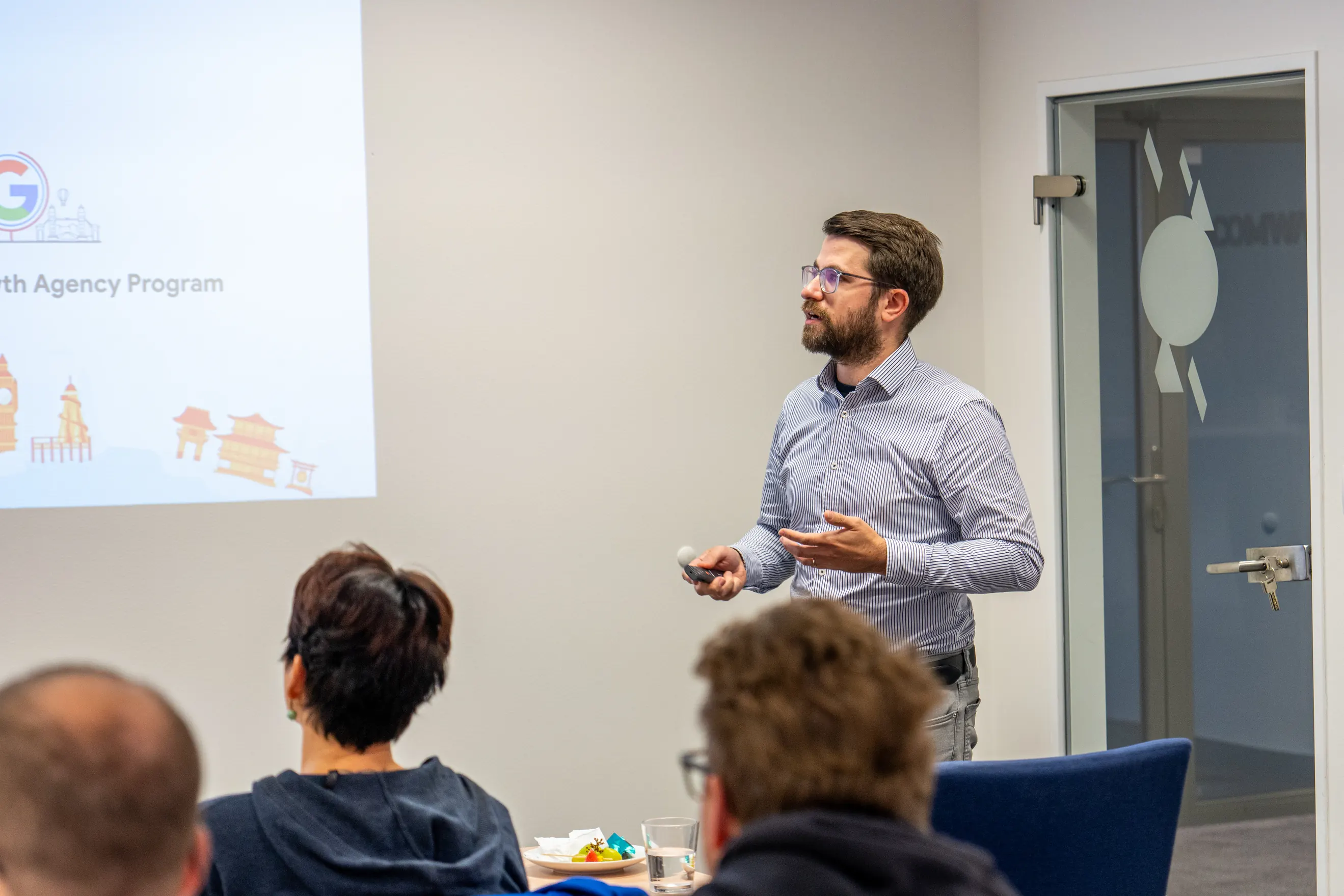 Přednášející před projekcí a účastníci u stolu na snídani ACOMWARE